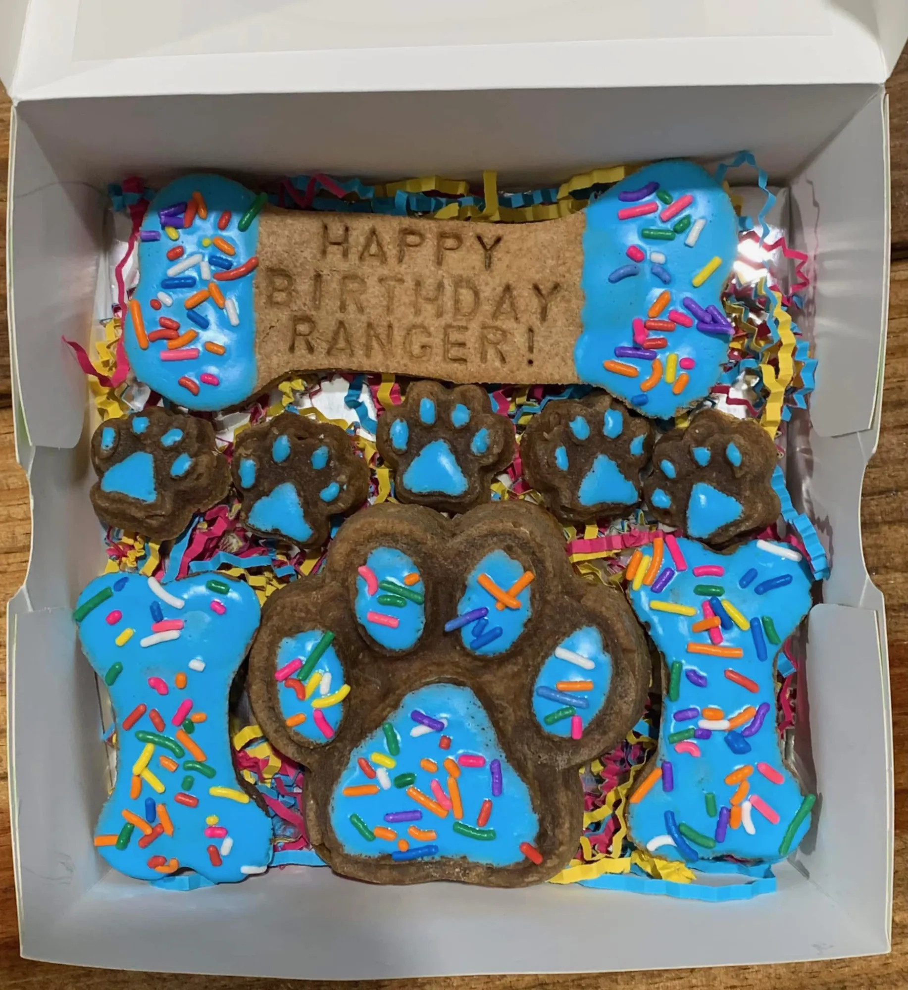 Dog birthday treat box with blue iced bones and paw cookies and rainbow sprinkles