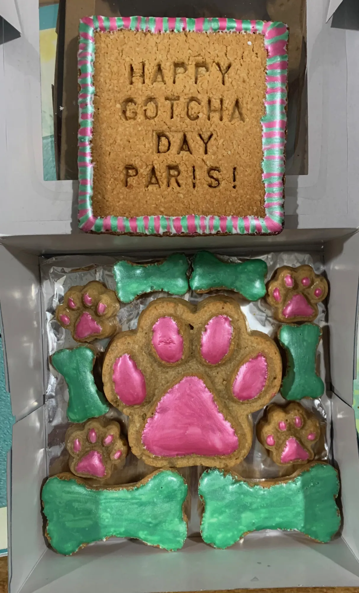 Gotcha day dog treats with a pink iced paw and green bones in a gift box