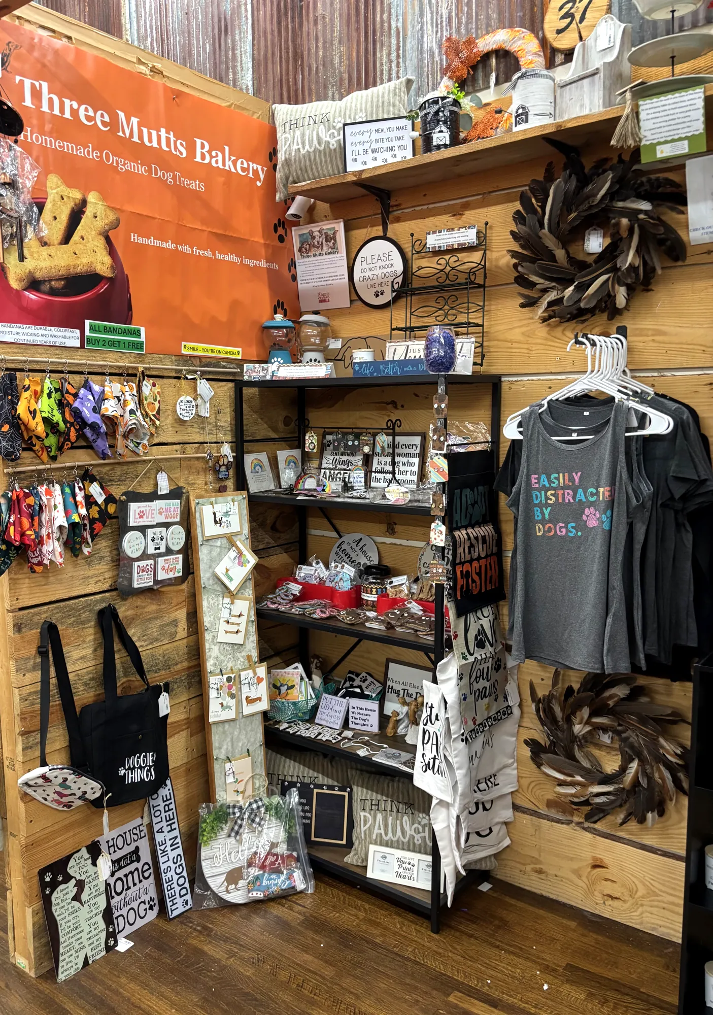 The Three Mutts Bakery booth inside Just Around The Corner, with the orange banner and shelves of organic dog treats and dog merch